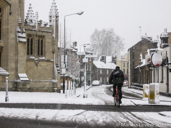 Man cycling through the snow in Cambridge.